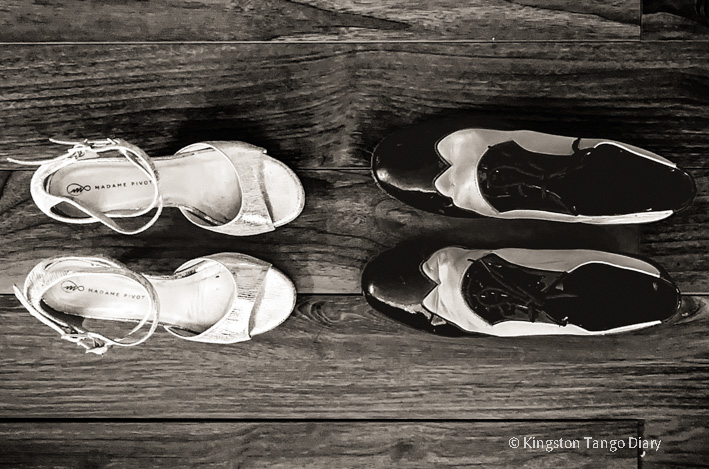 A pair of white woman dancing shoes and a pair of black-and-white man dancing shoes on a wooden floor